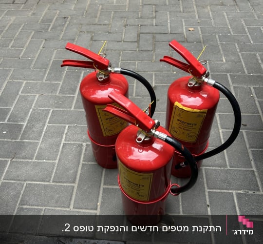שלושה מטפי כיבוי אש אדומים עם מדבקות בדיקה ותקינות